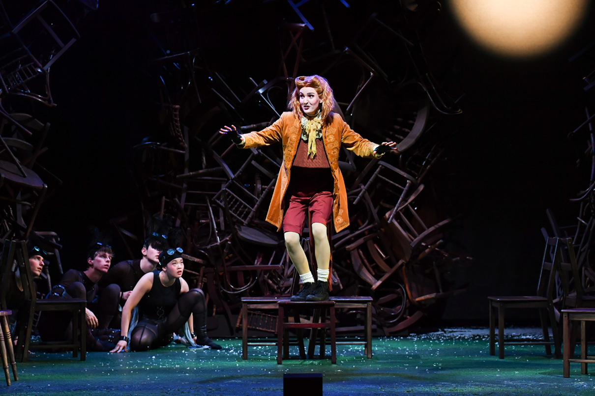 A singer dressed in costume, standing on a still, singing on a stage.